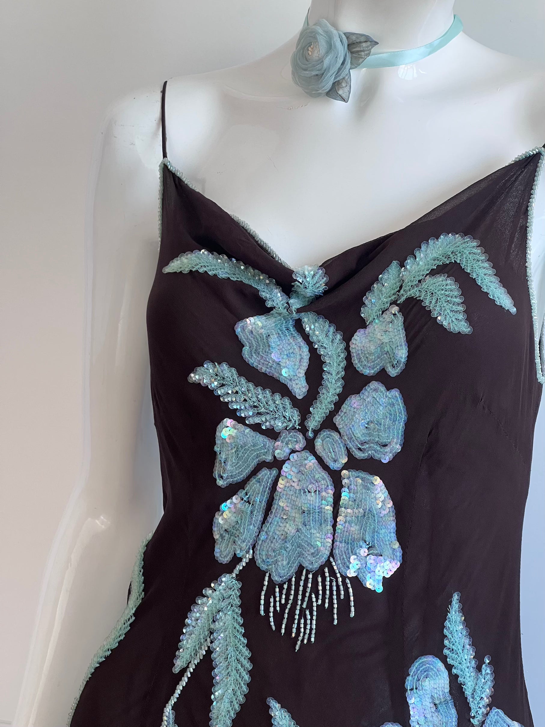 Mannequin wearing a black dress with blue floral embroidery on a plain background