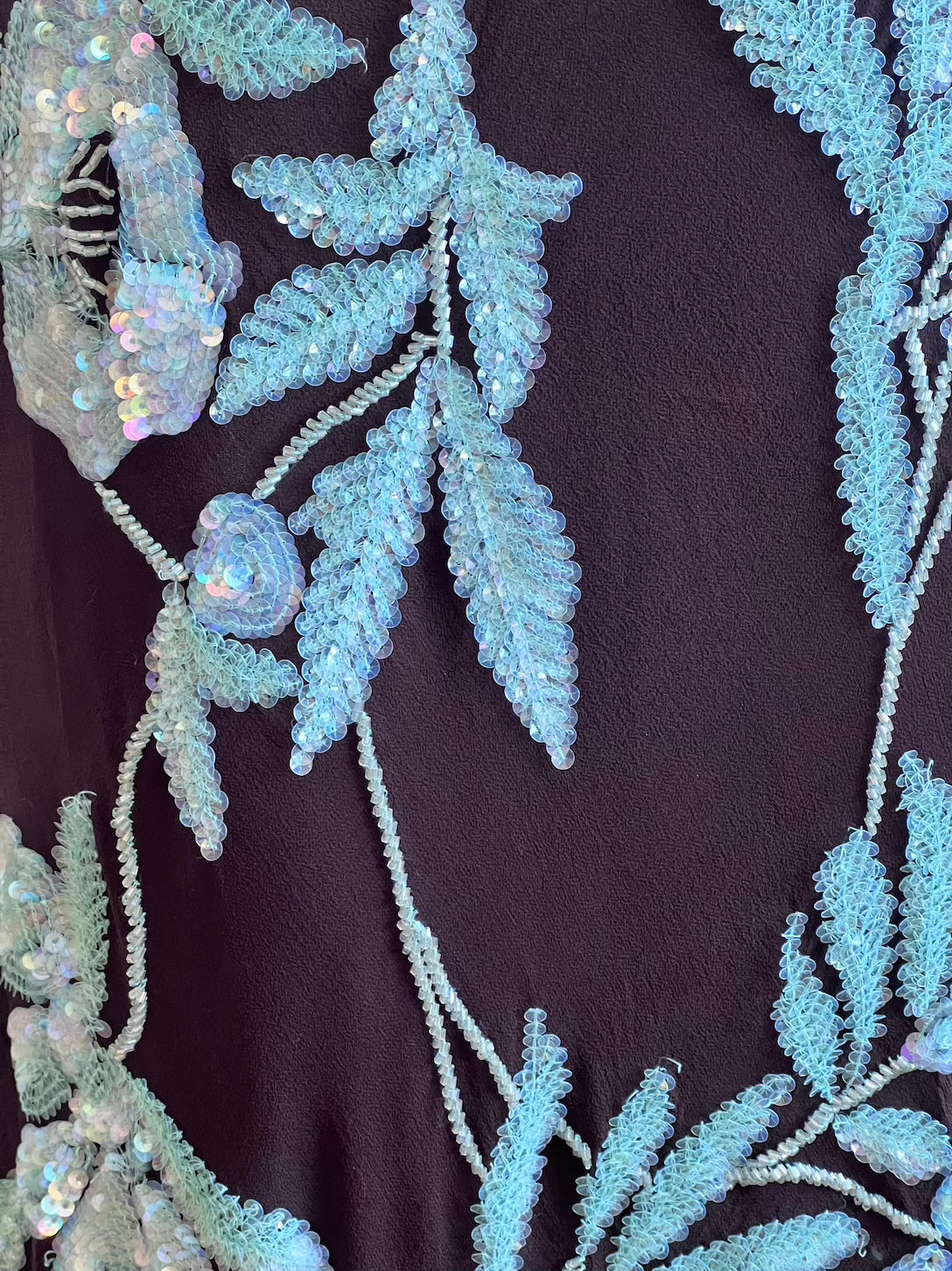 Close-up of decorative fabric with embroidered leaves and sequins on a dark background