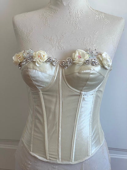 White corset with floral and embellishment details on a mannequin against a plain background