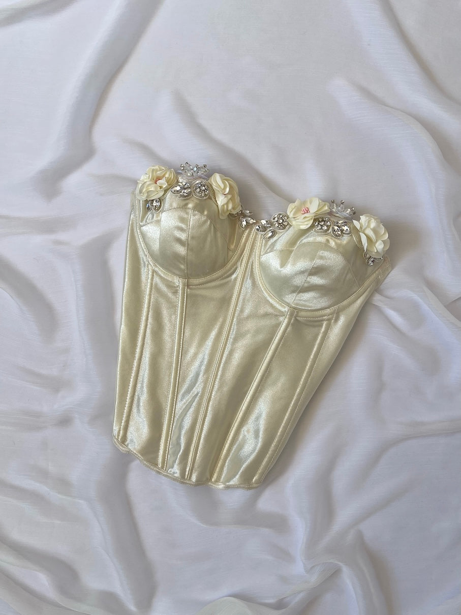 Cream-colored corset with floral and bead embellishments on a white fabric background